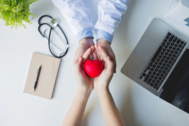 vue-dessus-docteur-patient-mains-tenue-coeur-rouge-table-blanche_38391-541